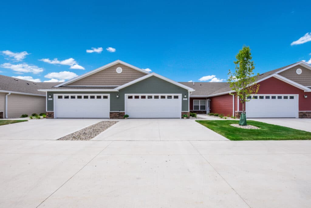 Row of modern townhouses with attached garages, each painted in different colors including green, beige, and red. The homes have a clean, minimalistic exterior design and a clear blue sky background.