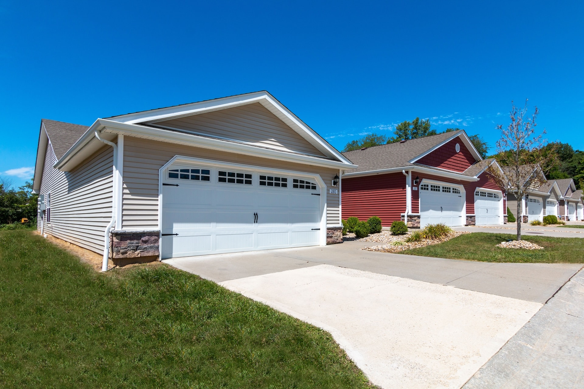 Row of suburban houses with garages and landscaped lawns under a clear blue sky.