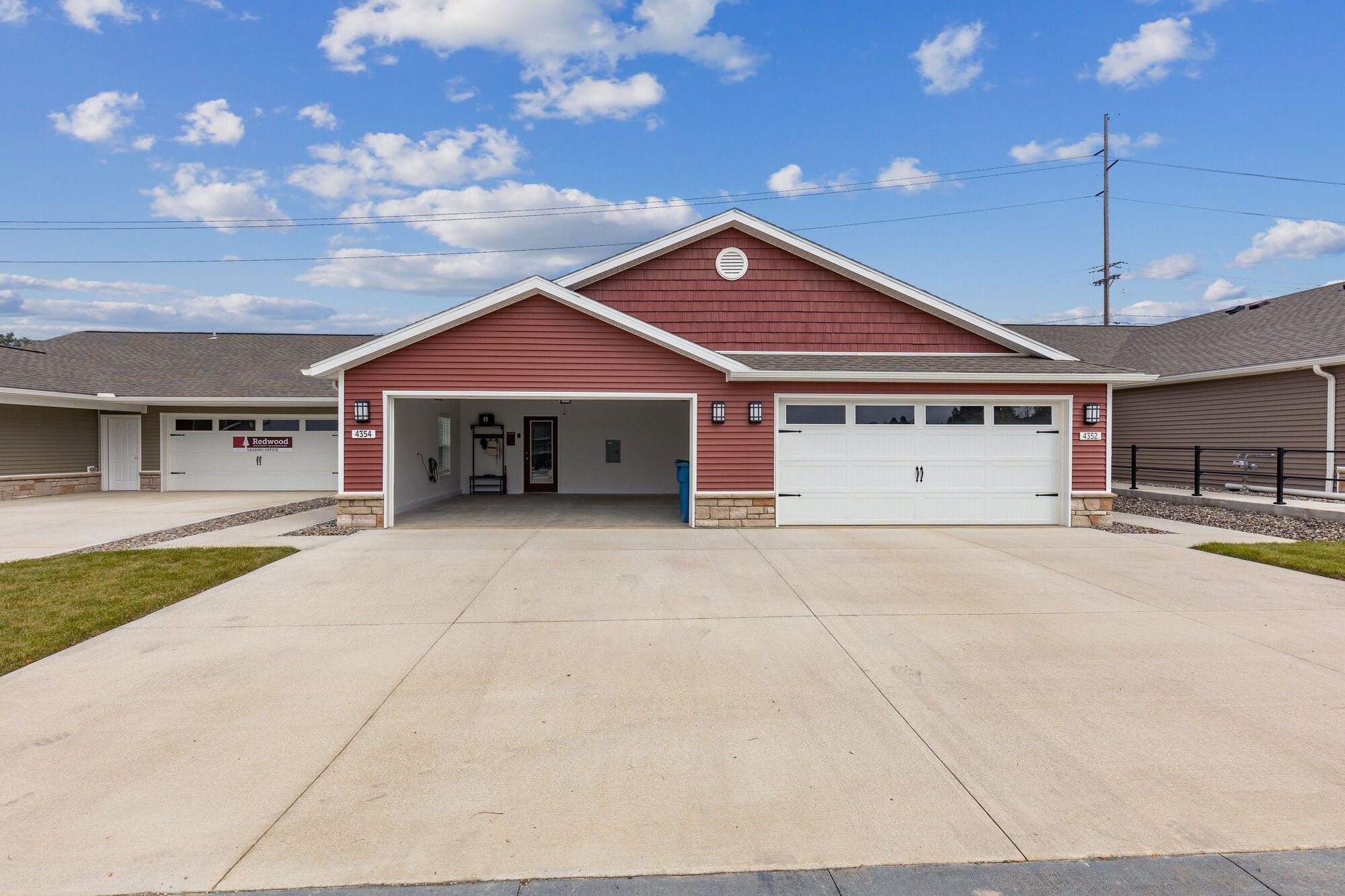 A red house with a double garage, white trim, concrete driveway, under a partly cloudy sky.