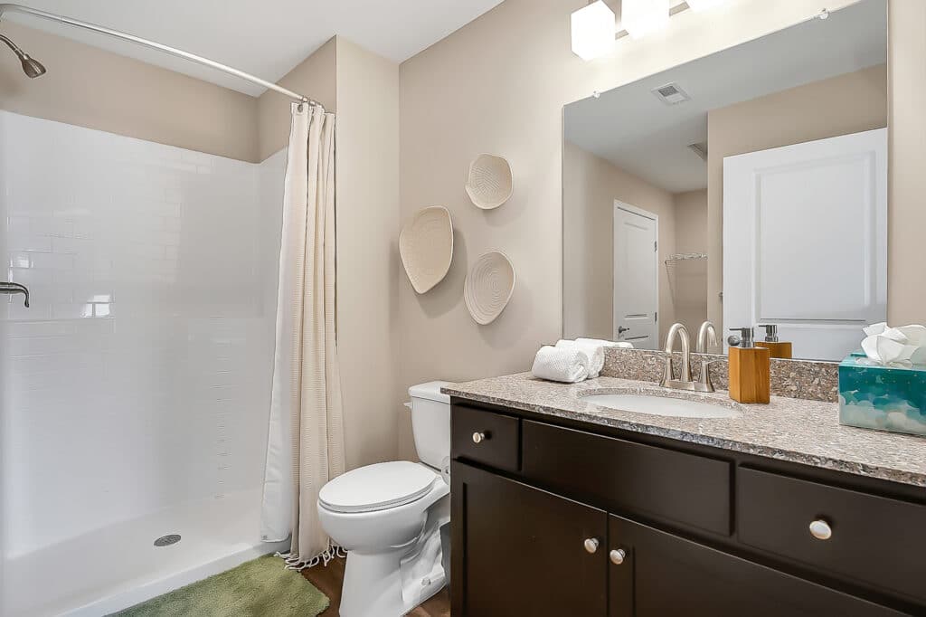 A modern bathroom with a shower, toilet, and vanity. The vanity includes a sink, towels, tissue box, and soap dispenser.Three decorative items are mounted on the wall above the toilet.