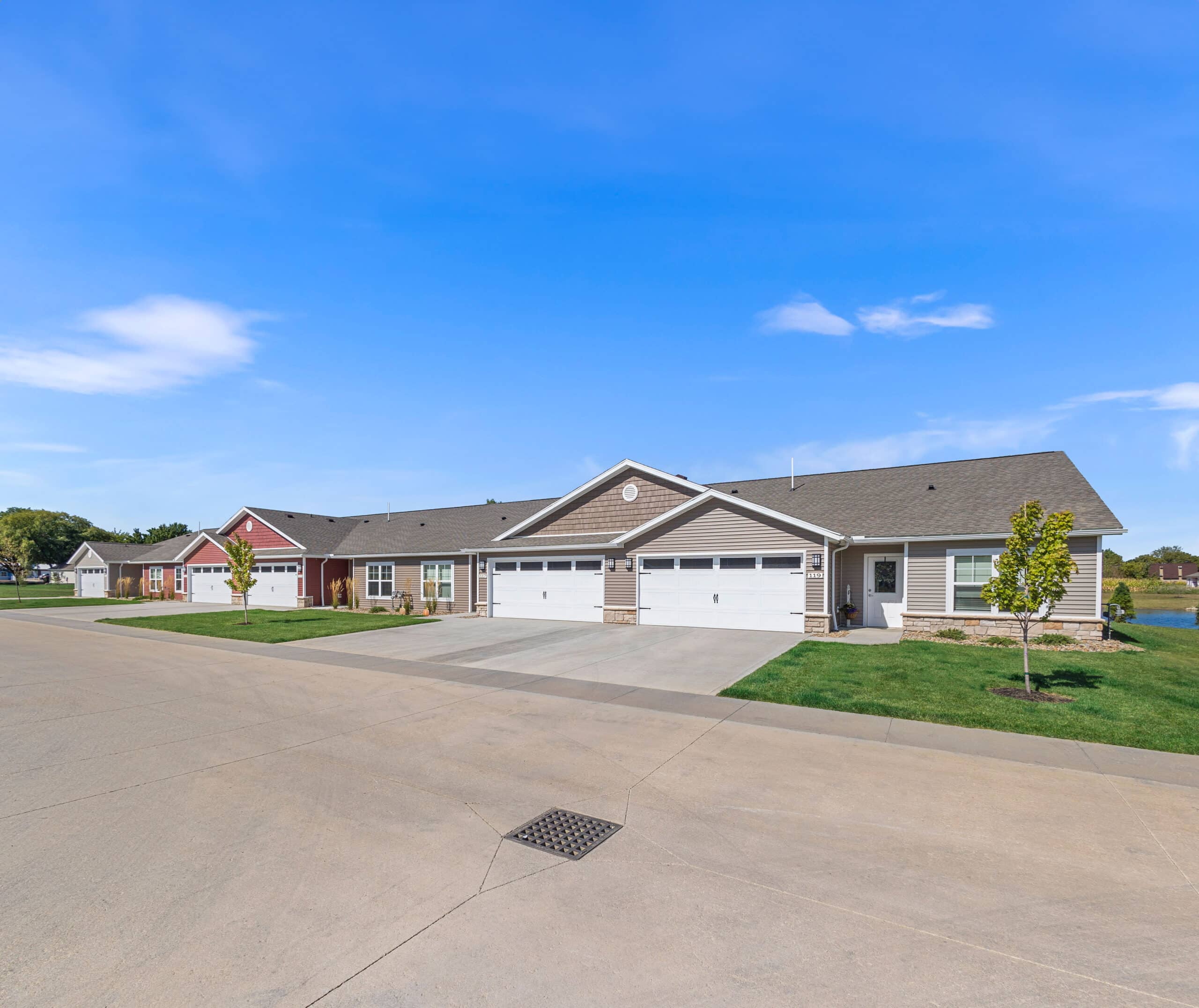 Row of modern single-story homes with garages on a suburban street under a clear blue sky.