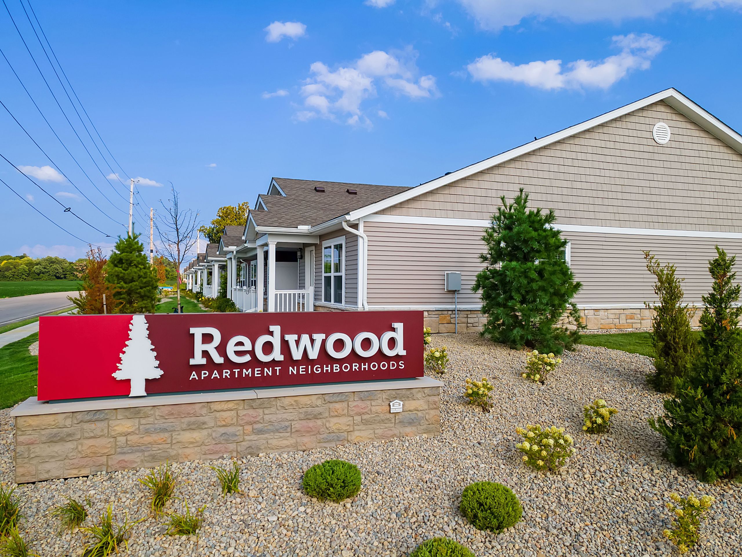 A sign reading "Redwood Apartment Neighborhoods" is displayed in front of single-story residential buildings with landscaping and a clear sky.