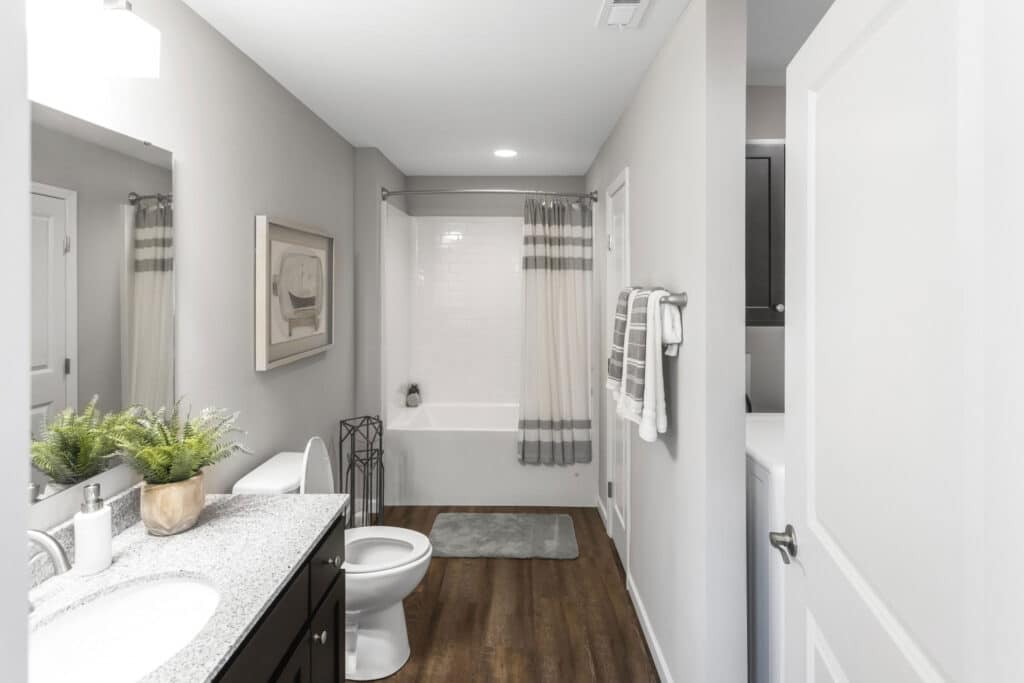 Modern bathroom with a granite countertop, sink, potted plant, bathtub with shower curtain, towel rack, wall art, and wood-look flooring.