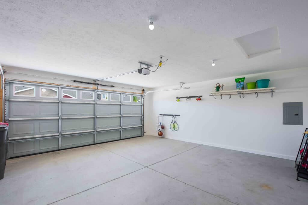 Clean, empty two-car garage with white walls, overhead lighting, and a few items stored on shelves and hooks along the right wall.