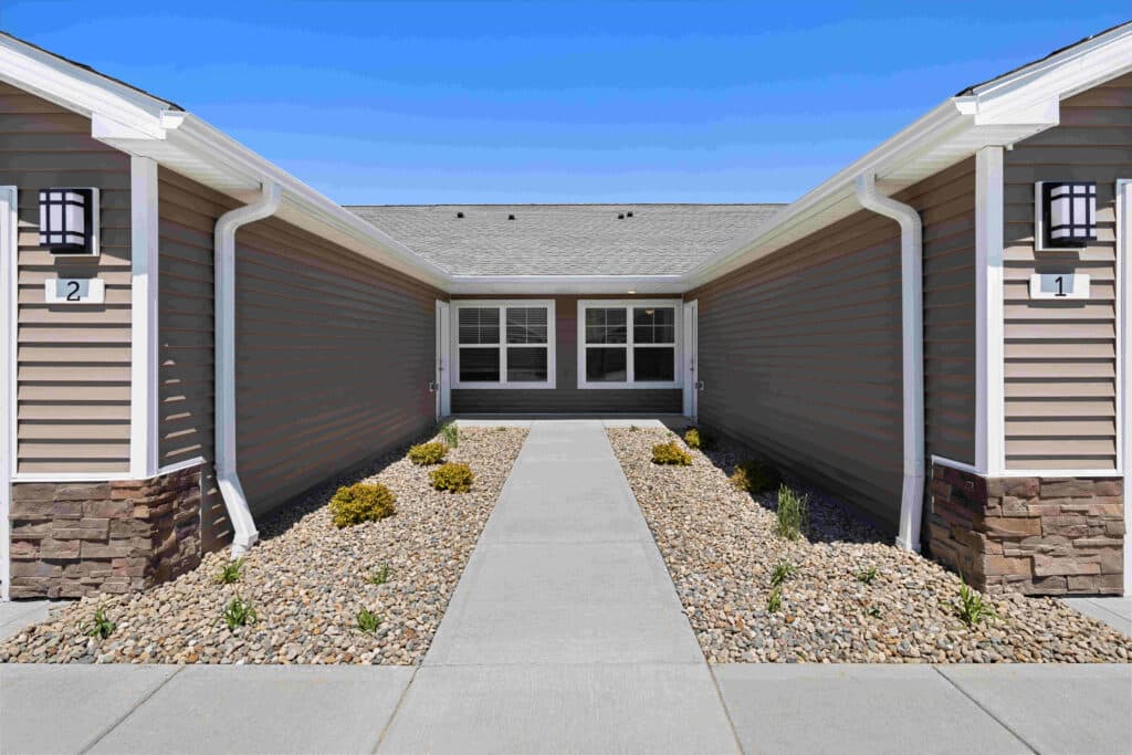 Sidewalk leading to a building entrance flanked by two walls with small rocks and plants on both sides under a clear blue sky.
