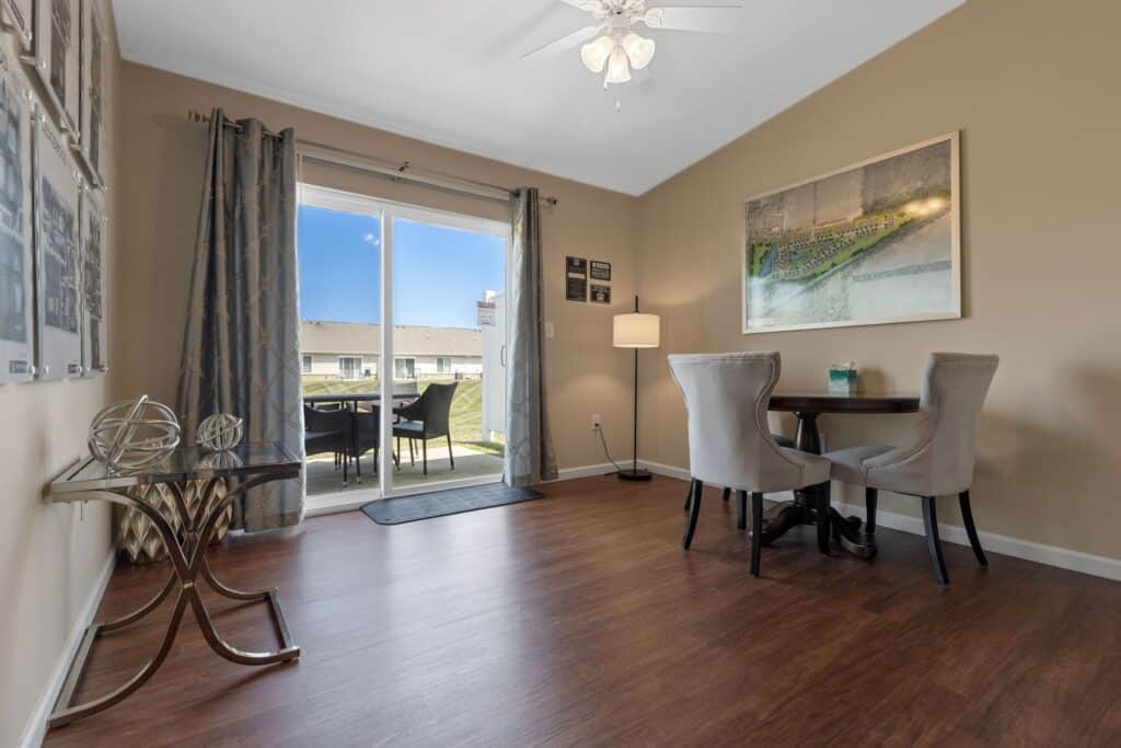 Dining area with two chairs and a small round table, large wall art, wood flooring, and sliding glass doors leading to an outdoor patio with chairs.