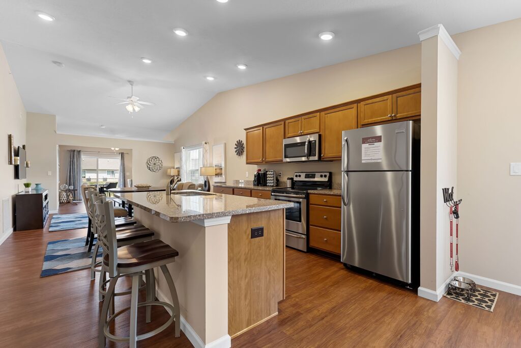 Modern kitchen with stainless steel appliances, wooden cabinets, and granite countertops, connected to a dining area and living space with wooden flooring and neutral walls.