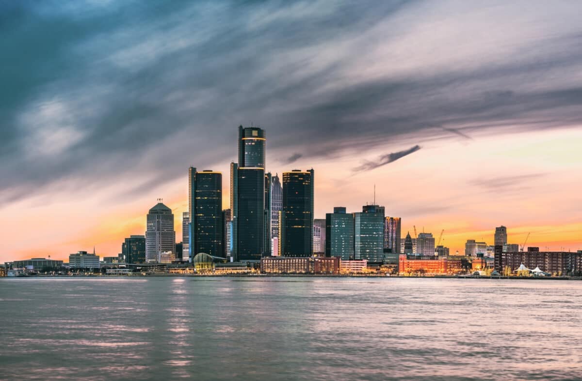 City skyline with tall skyscrapers near a waterfront at sunset, under a partly cloudy sky.
