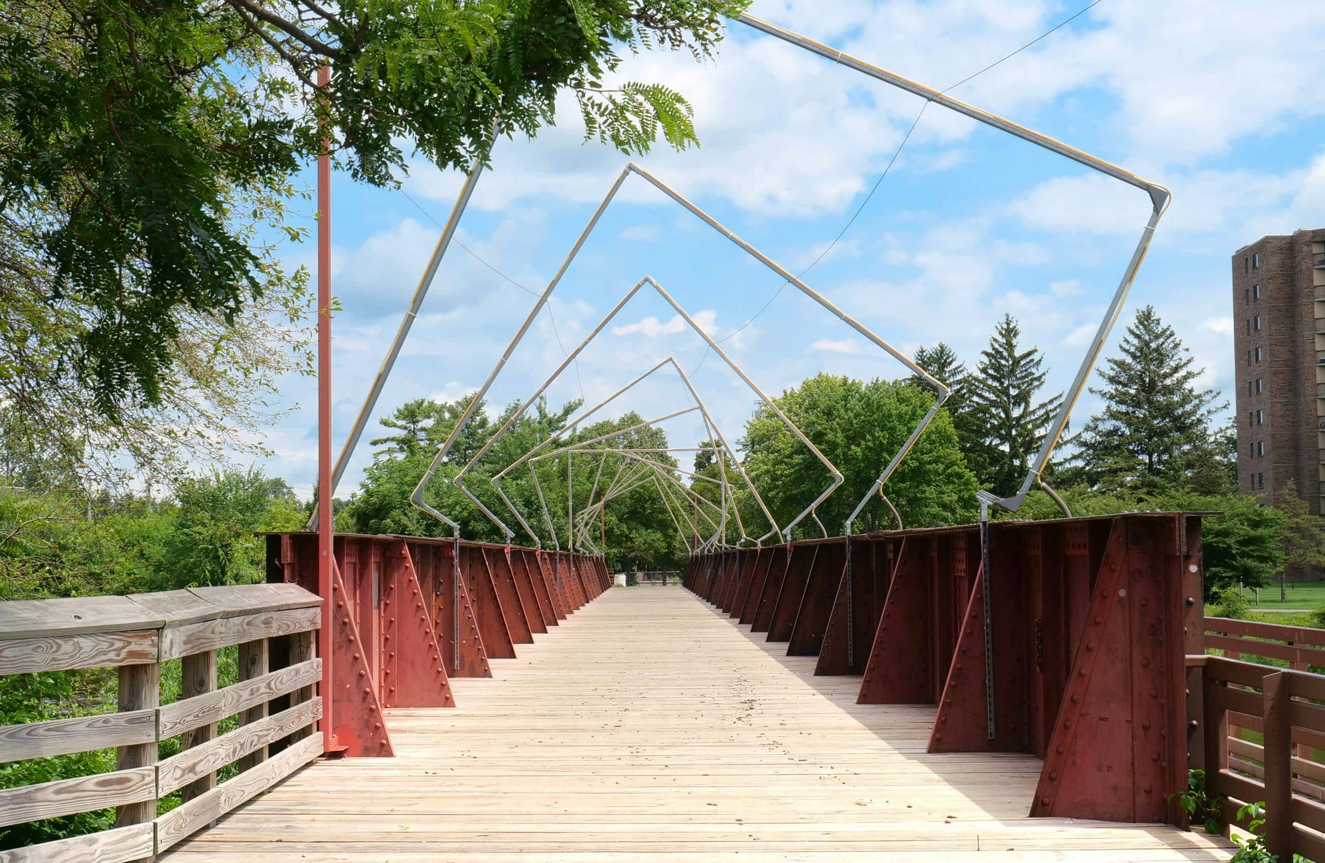 Artistic footbridge in downtown Lansing, Michigan with metal and wood structure on a sunny day.