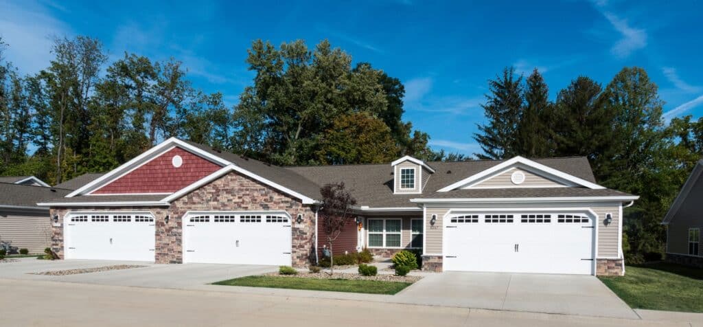 A duplex house with two garages, each with a driveway, surrounded by trees and a clear blue sky.