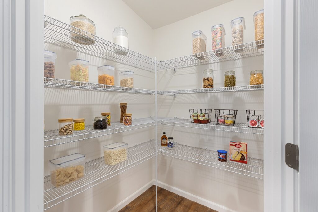 A walk-in pantry with white wire shelves holds various food items in clear containers and jars, organized neatly along the walls.