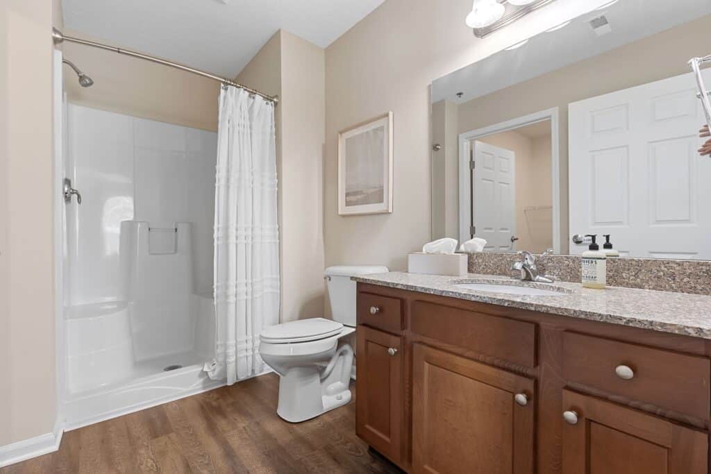 Bathroom with a walk-in shower, white shower curtain, toilet, wooden vanity with granite countertop, sink, mirror, and tissue box on the counter.