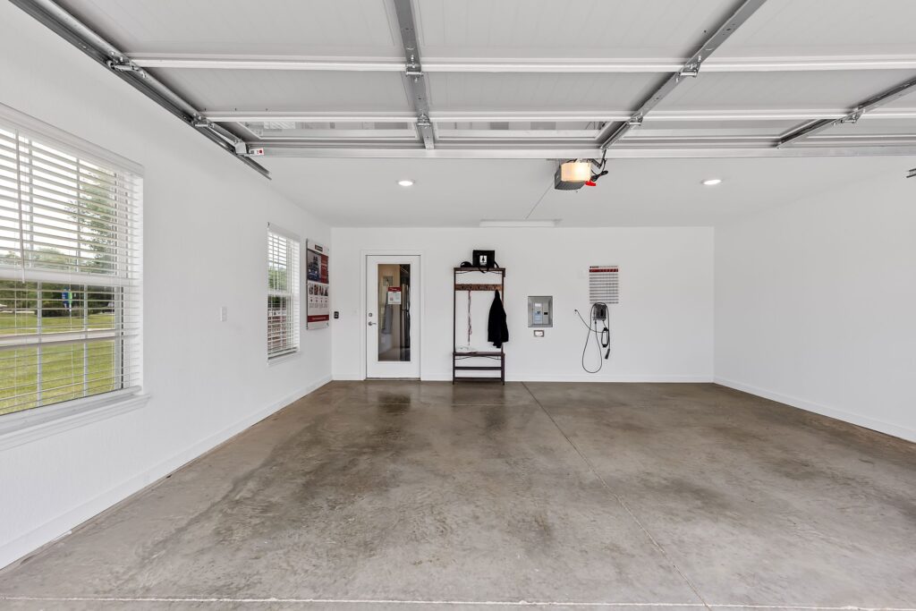 Clean, empty garage with polished concrete floor, white walls, wall-mounted equipment, a coat rack, and two windows letting in natural light.