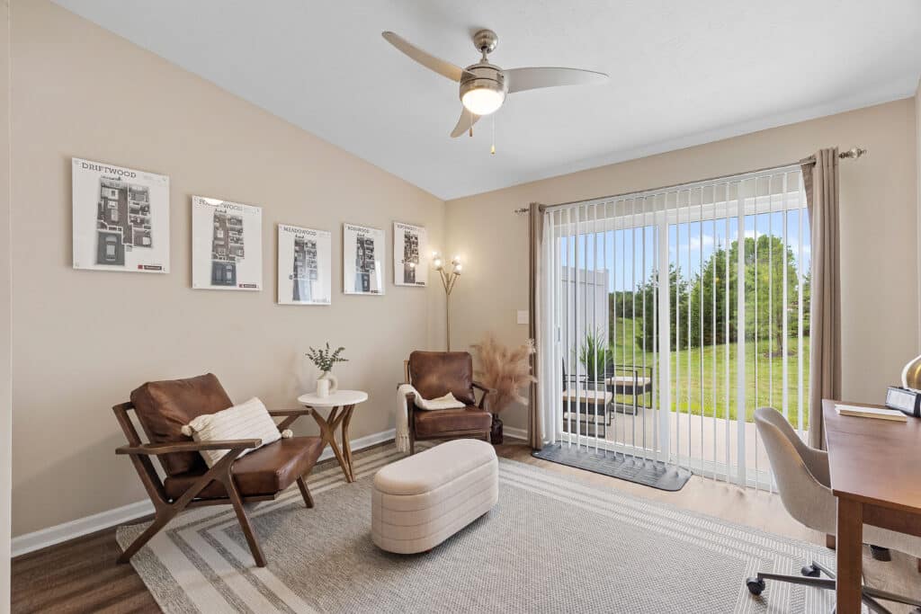 Home office with two chairs, a small ottoman, a desk, a ceiling fan, wall art, floor lamp, and sliding glass doors opening to a patio and yard.