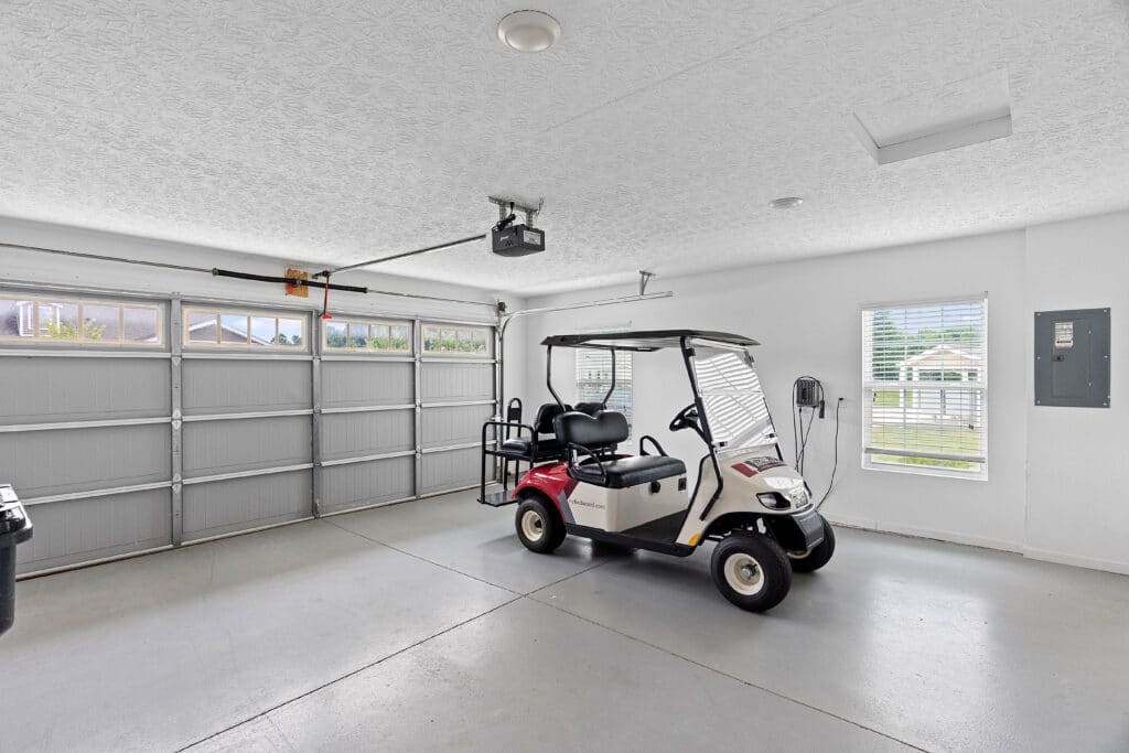 A white and red golf cart is parked inside a clean, spacious garage with gray floors, white walls, and large windows letting in natural light.