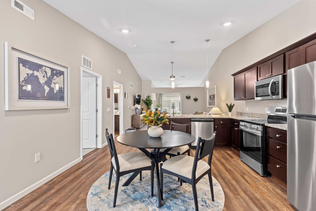 Modern apartment kitchen and dining area with stainless steel appliances, dark wood cabinets, a round table with four chairs, and a world map on the wall.
