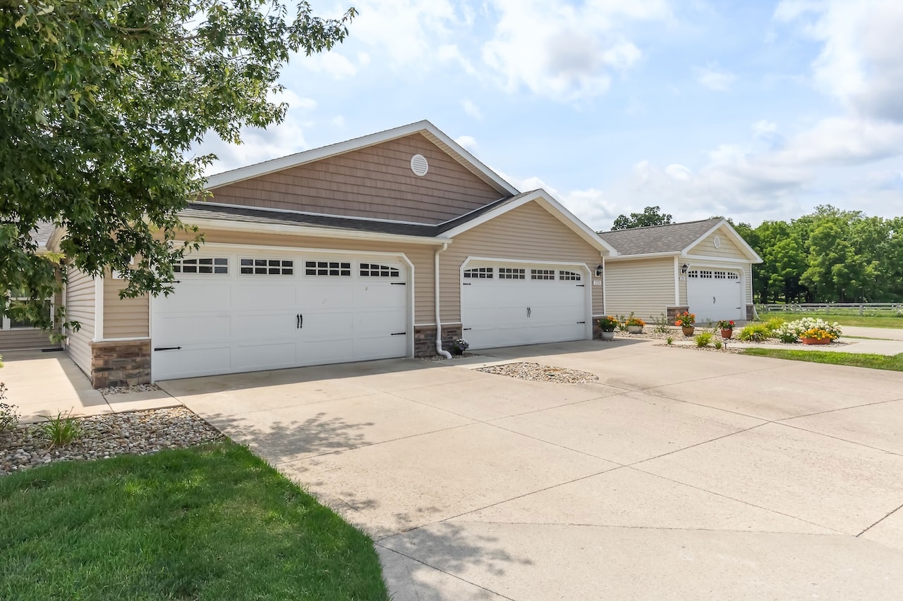 Row of attached beige garages with white doors and stone accents, set along a wide concrete driveway on a sunny day.