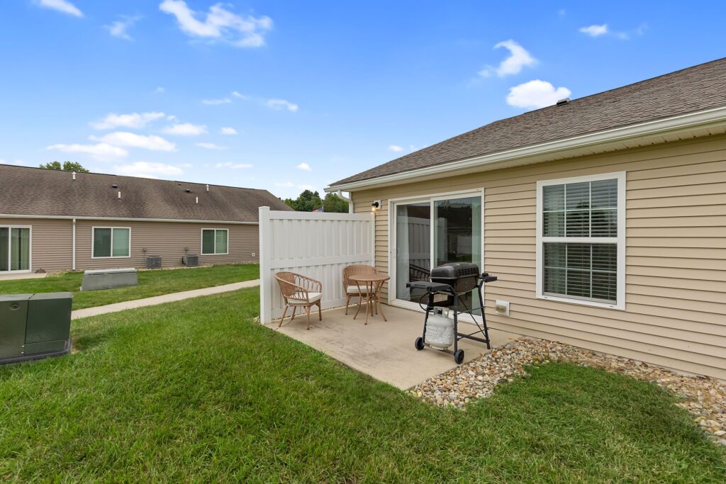 A house with a grill and chairs in front of it.