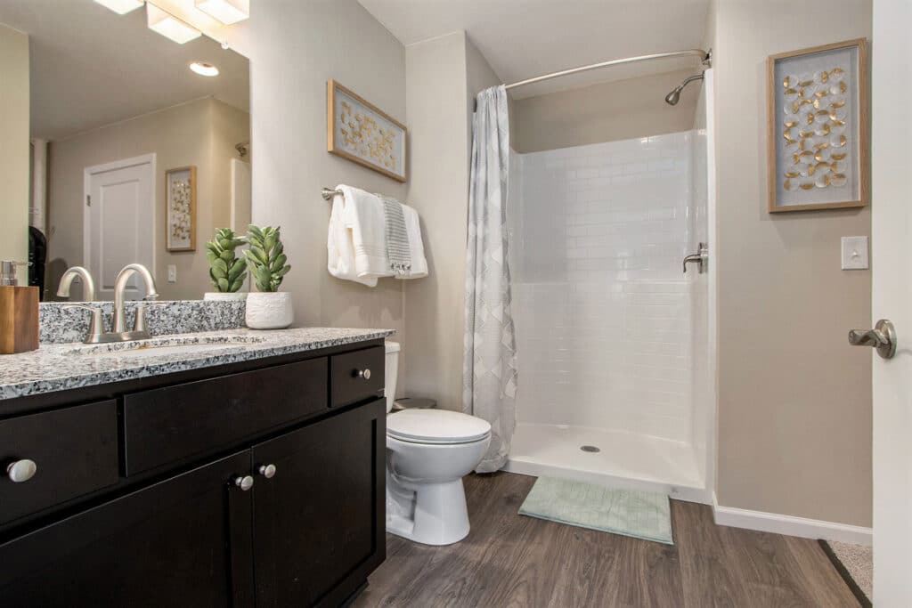 Modern bathroom with a dark wood vanity, granite countertop, white toilet, walk-in shower with white tiles, and decorative wall art.