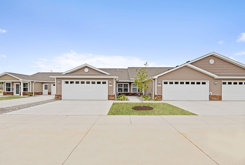Single-story duplex homes with attached two-car garages, beige siding, and paved driveways under a clear blue sky.