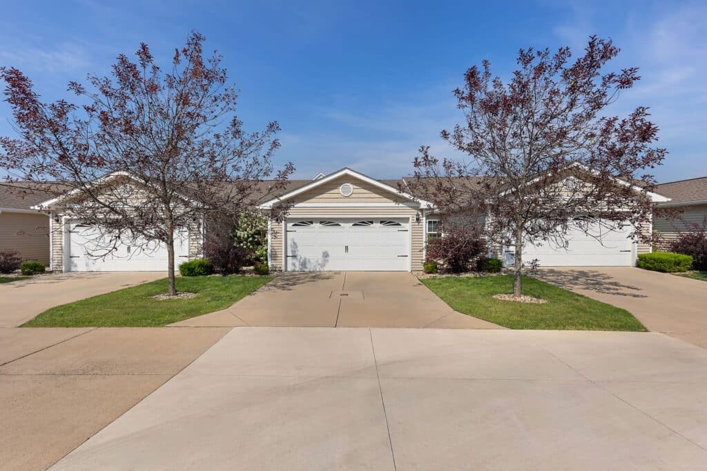 Three attached, single-story suburban houses with garages, situated side by side, each with driveways and small front yards containing young trees.