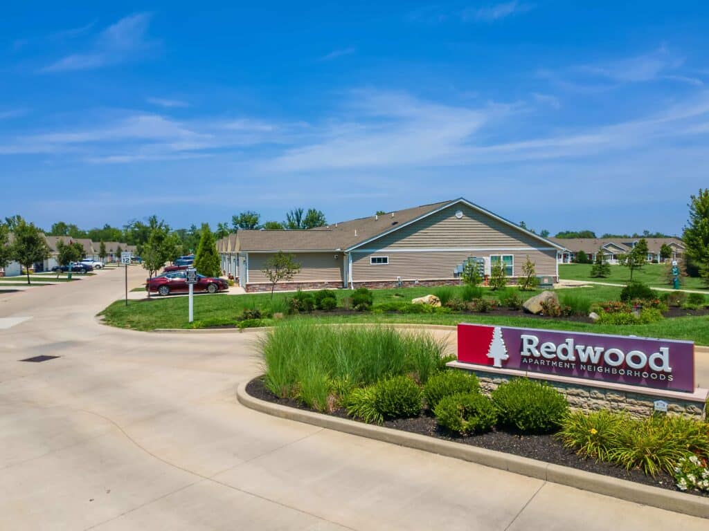 Redwood Apartment Neighborhoods entrance sign with a landscaped area and single-story apartment building under a clear blue sky.