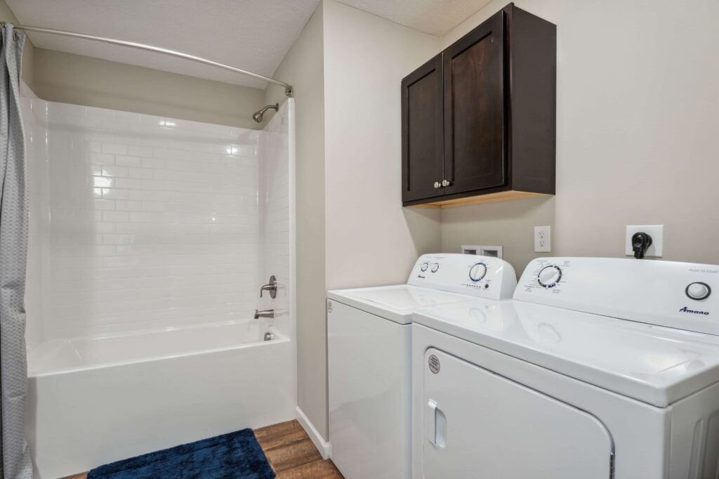 Bathroom with a white bathtub and shower curtain on the left, and a washer and dryer set with dark wall cabinets above on the right.