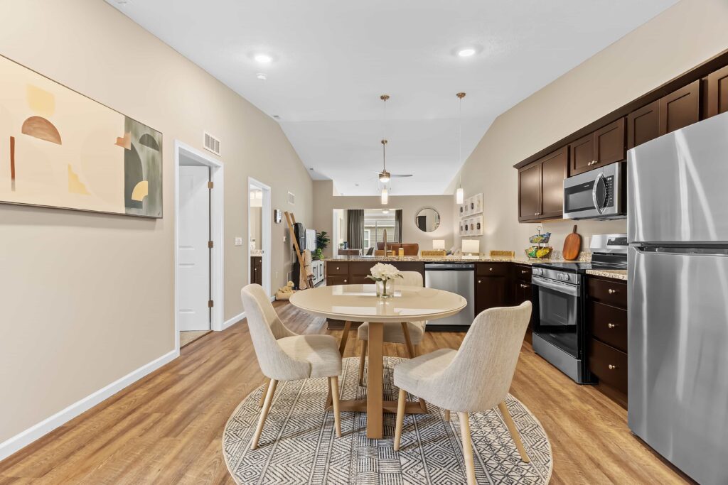 Modern open-concept kitchen and dining area with wood flooring, round dining table, beige chairs, dark wood cabinets, and stainless steel appliances.