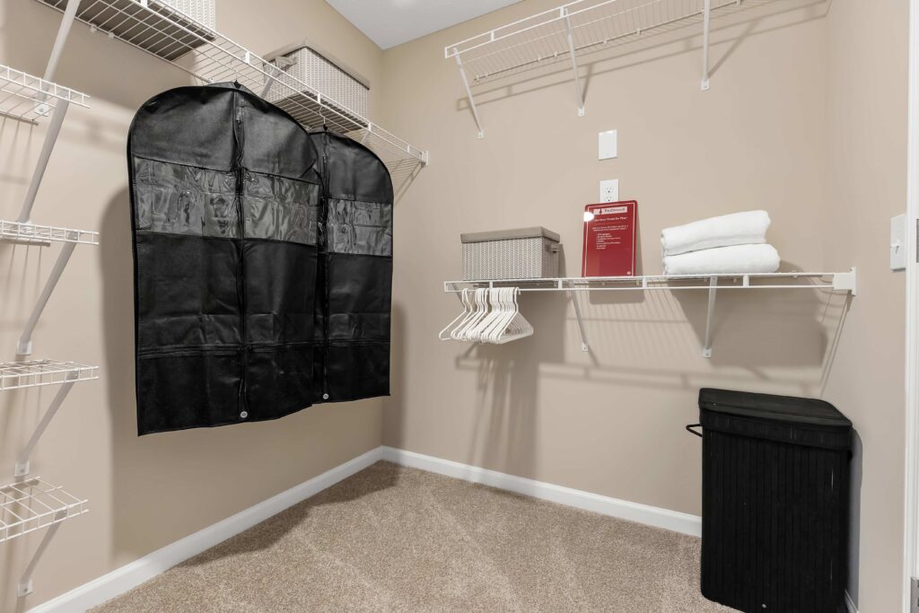 A walk-in closet with wire shelves, storage bins, hangers, a garment bag, folded towels, and a laundry hamper on carpeted flooring.