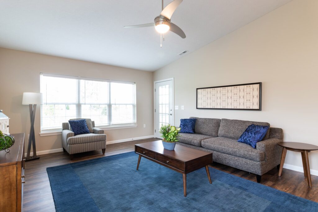 A modern living room with a gray sofa, blue rug, wooden coffee table, armchair, large window, and neutral walls.
