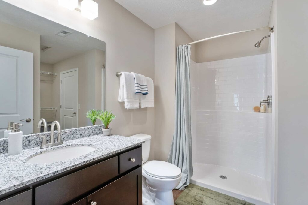 Modern bathroom with a granite countertop, dark wood vanity, toilet, walk-in shower with a curtain, and folded towels on a wall rack.