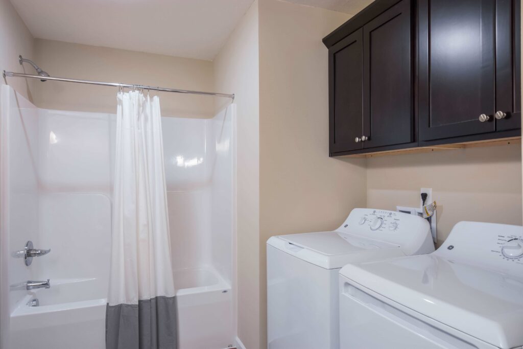 Bathroom with a white bathtub and shower curtain on the left, and a white washer and dryer set with dark cabinets above on the right.