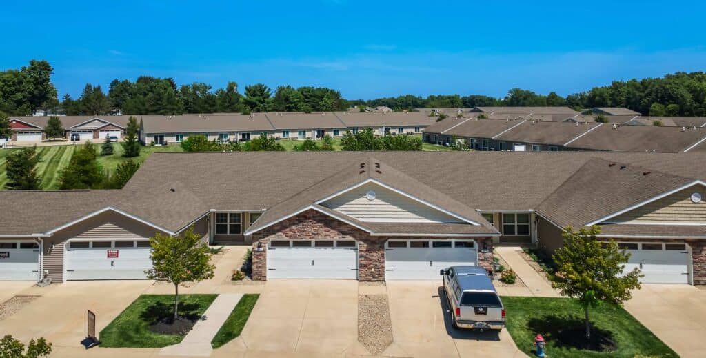 A row of suburban single-story houses with attached garages, driveways, and well-maintained lawns under a clear blue sky.