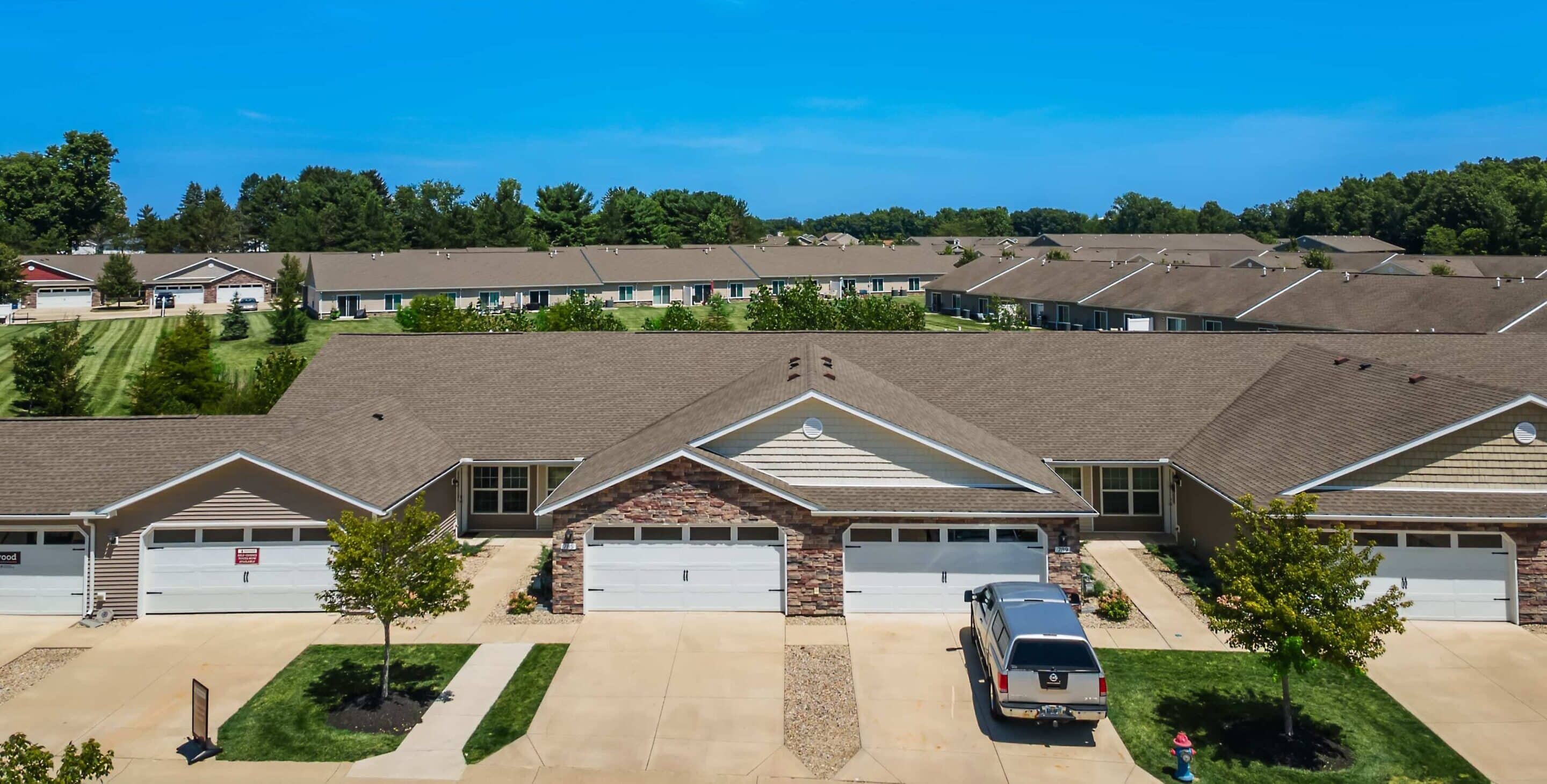 A row of suburban single-story houses with attached garages, driveways, and well-maintained lawns under a clear blue sky.