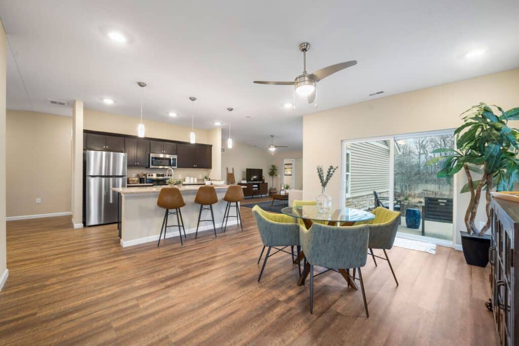 Open-concept kitchen, dining, and living area with wood flooring, modern appliances, bar stools, round dining table, and sliding glass doors leading to an outdoor patio.