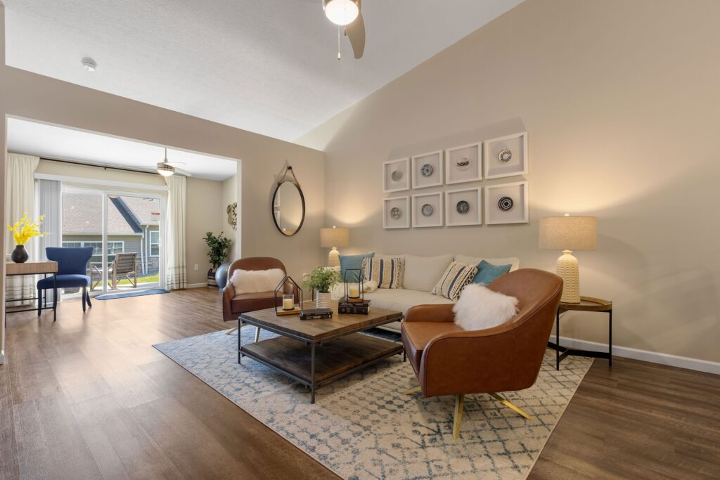 A modern living room with two brown chairs, a beige sofa, a coffee table, lamps, wall art, and large window opening to a patio.