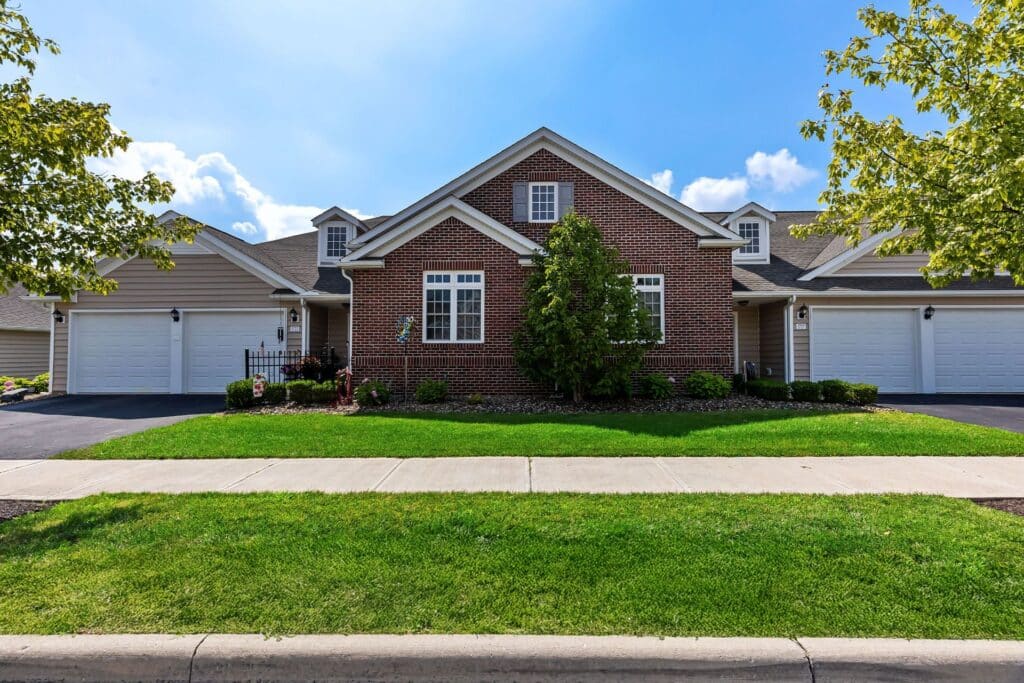 Single-story brick and siding duplex with two driveways, each leading to a double garage, and a well-maintained lawn and landscaping in front.