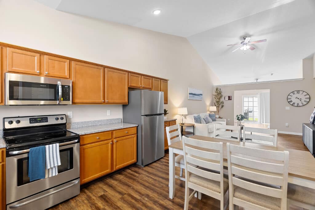 Modern kitchen and living area with wood floors, stainless steel appliances, light wood cabinets, and a dining table with chairs in an open layout.