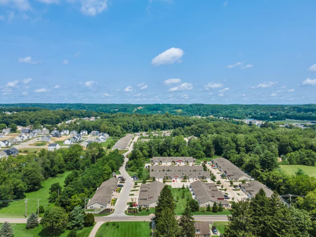 Aerial view of a suburban neighborhood with houses, streets, and green trees under a clear blue sky.