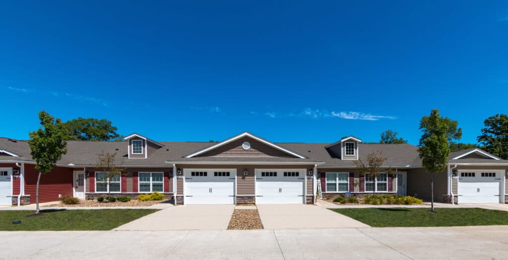 A row of modern single-story townhouses with attached garages, small front yards, and clear blue sky above.