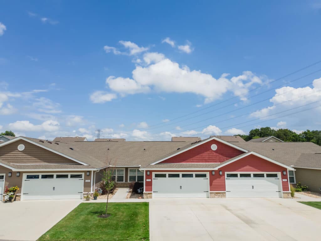 Row of modern suburban townhouses with attached garages under a blue sky with scattered clouds.