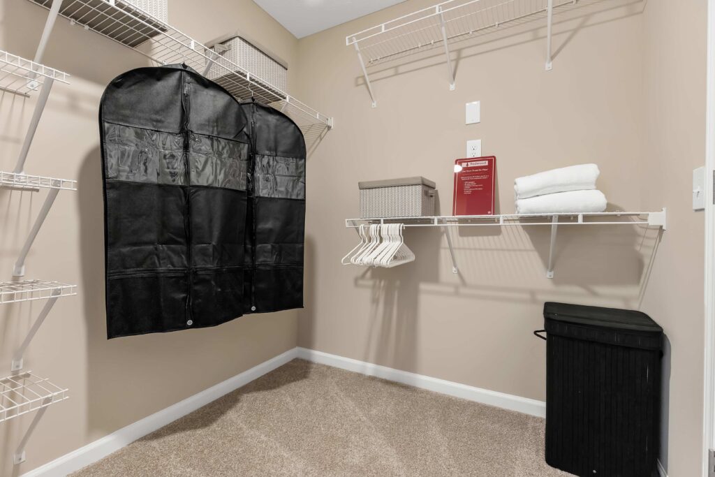 A walk-in closet with wire shelves, a black garment bag, storage boxes, hangers, folded towels, a laundry basket, and a fire safety guide.