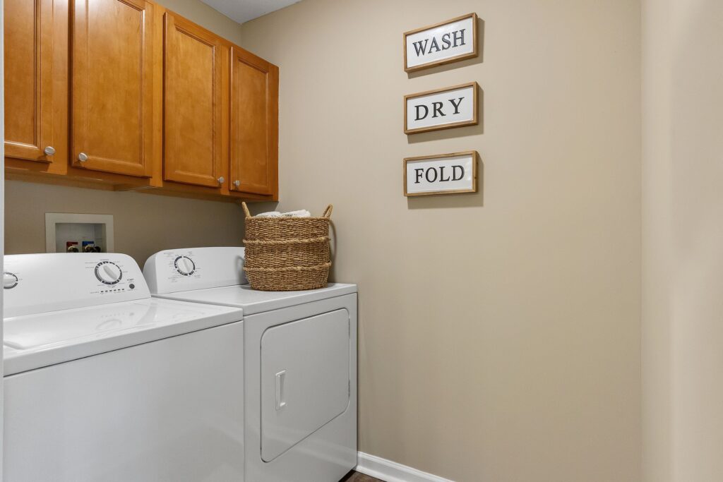 Laundry room with a washer and dryer, wooden cabinets, a wicker basket on the dryer, and three wall signs reading "WASH," "DRY," and "FOLD.