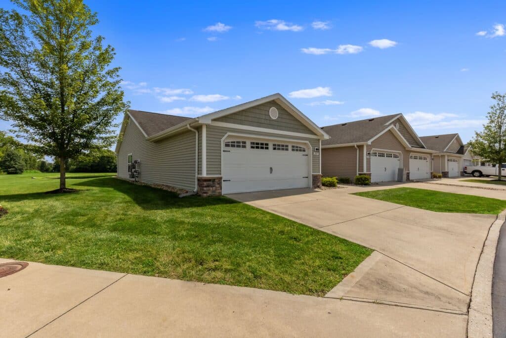 Single-story suburban houses with attached garages and well-kept lawns, lining a residential street on a clear day.