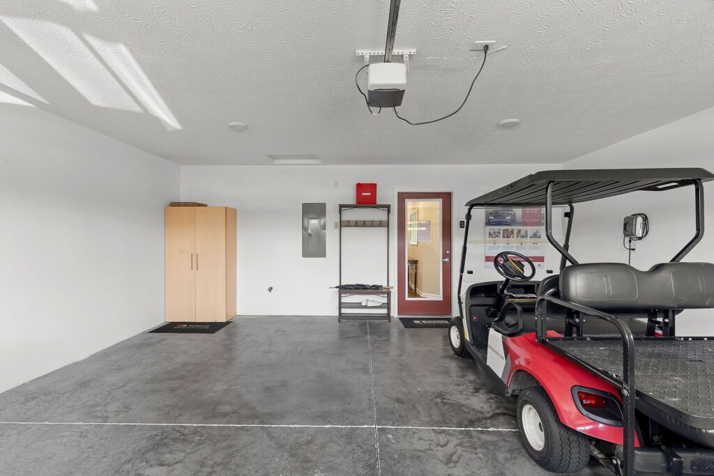 A clean garage with a red golf cart, a wooden cabinet, a metal shelf, and a door with a window leading outside.