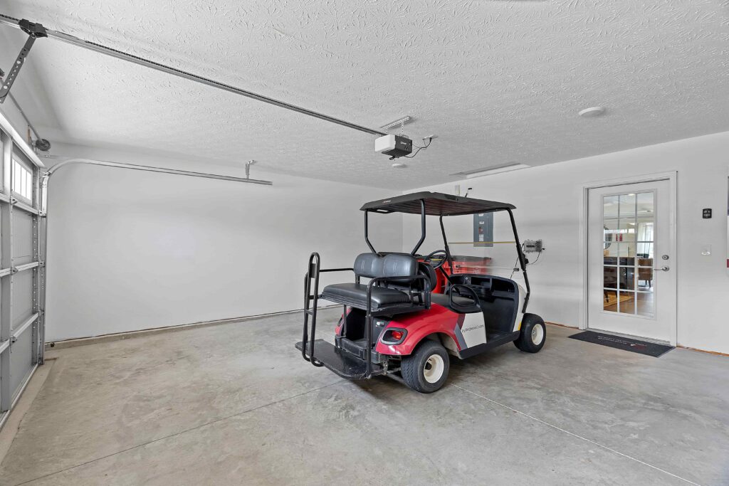 A red and black golf cart is parked inside a clean, empty garage with a concrete floor and white walls.