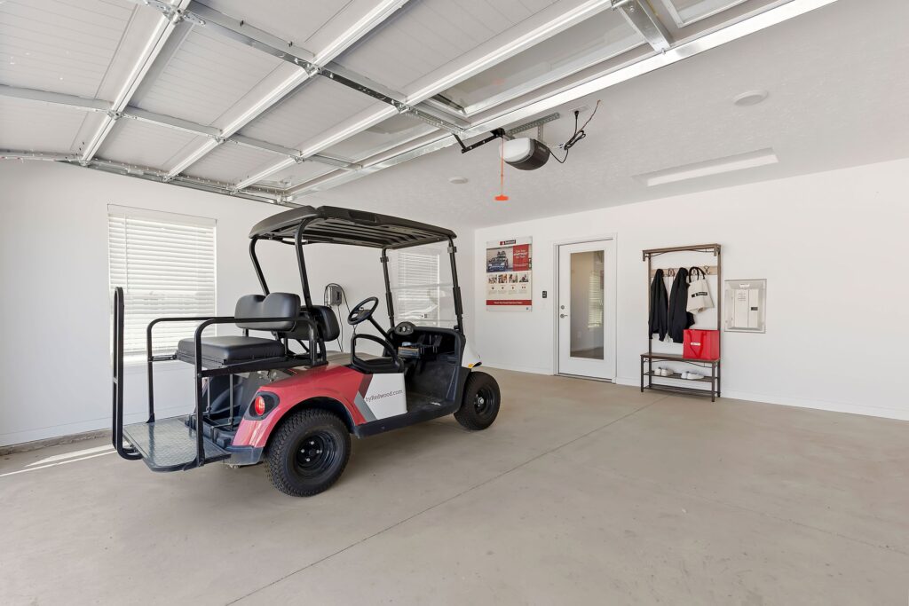 A red and black golf cart is parked inside a clean, organized garage with white walls, windows, and storage items on the wall.
