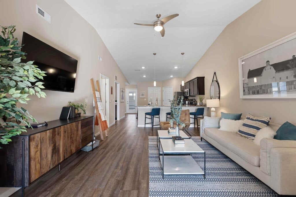 Modern open-concept living room and kitchen with neutral tones, wood flooring, a wall-mounted TV, beige sofa, dining area, and contemporary decor.