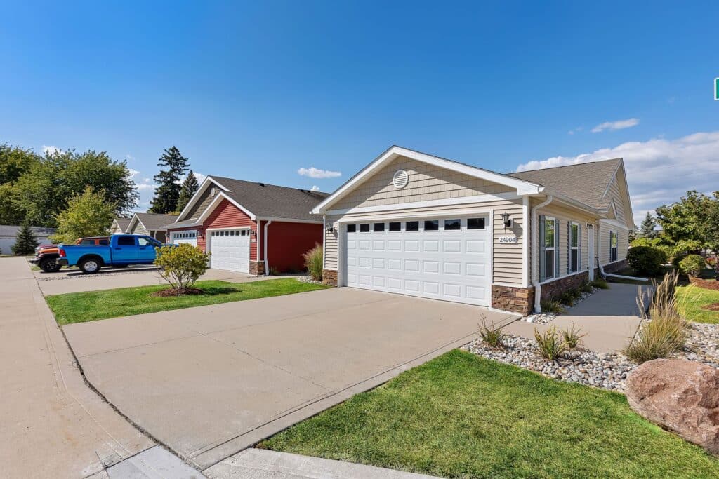 Single-story suburban homes with attached garages and well-maintained lawns on a sunny day; a blue truck is parked in one driveway.