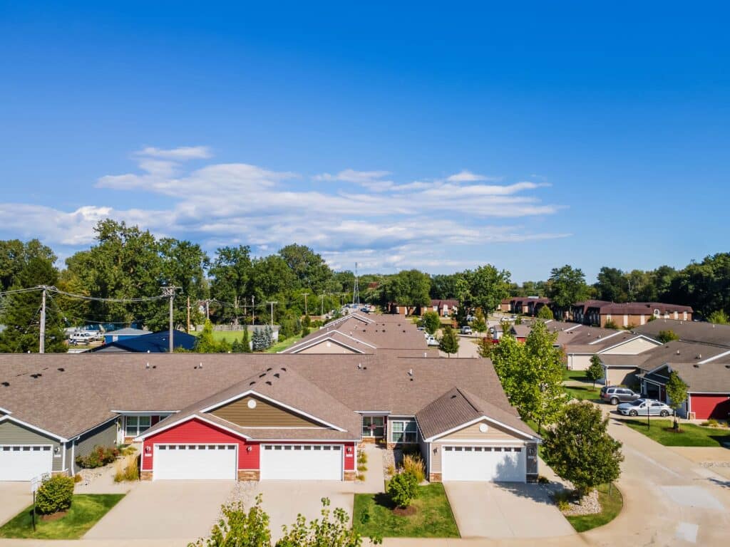 Aerial view of a suburban neighborhood with single-story houses, driveways, and well-maintained lawns under a clear blue sky.